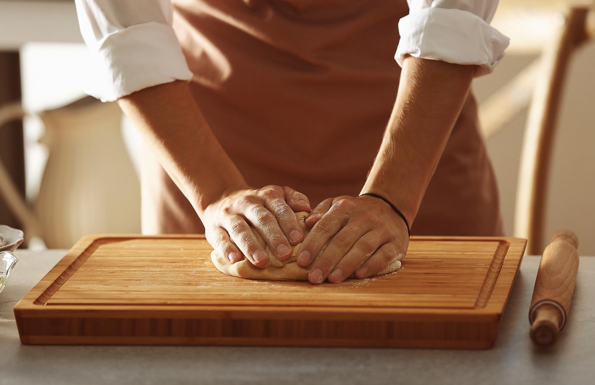 Hands preparing dough on wooden board